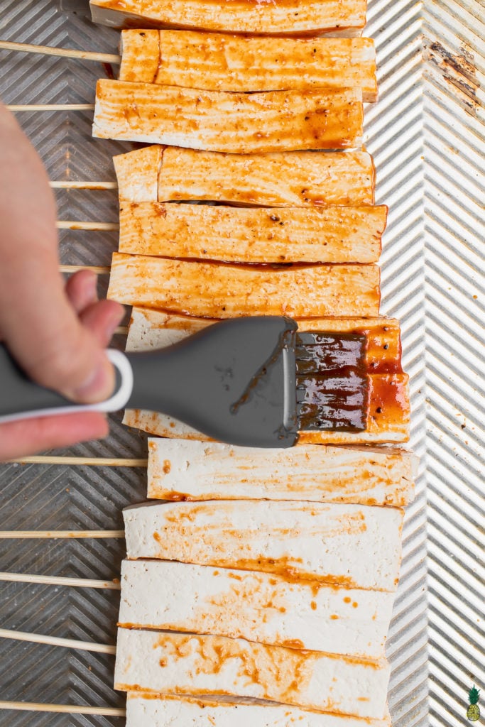 tofu skewers being brushed with barbecue sauce 
