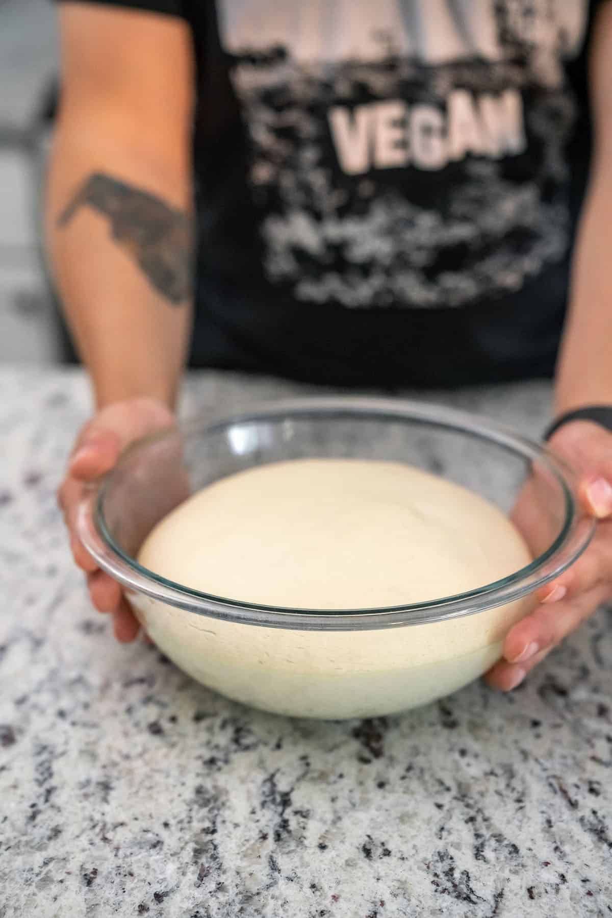 risen pizza dough in glass bowl