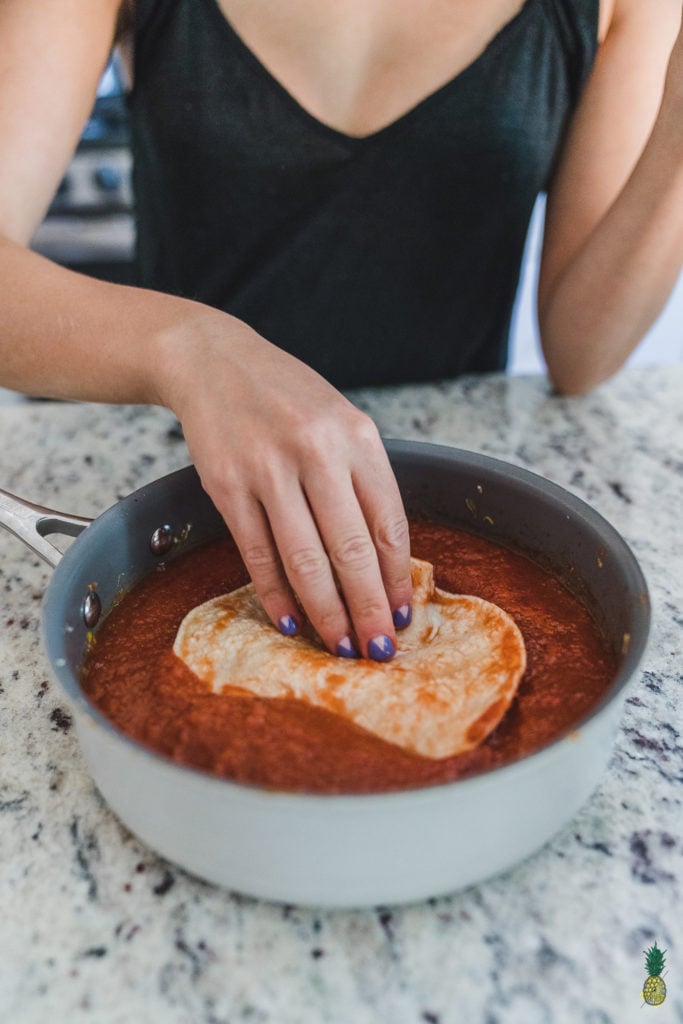 image of tortilla being dipped in homemade enchilada sauce. 