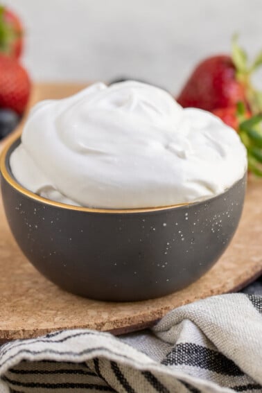 Bowl of fluffy coconut whipped cream next to berries by Sweet Simple Vegan