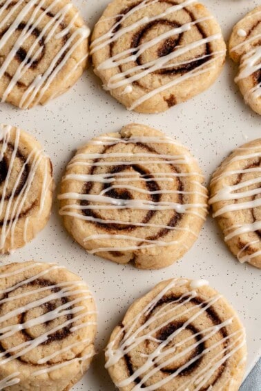 close up photo of cream cheese frosted cinnamon roll cookies on white plate