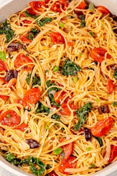close up of vegan pasta in a pot with tomatoes, kale, olives, basil and parmesan
