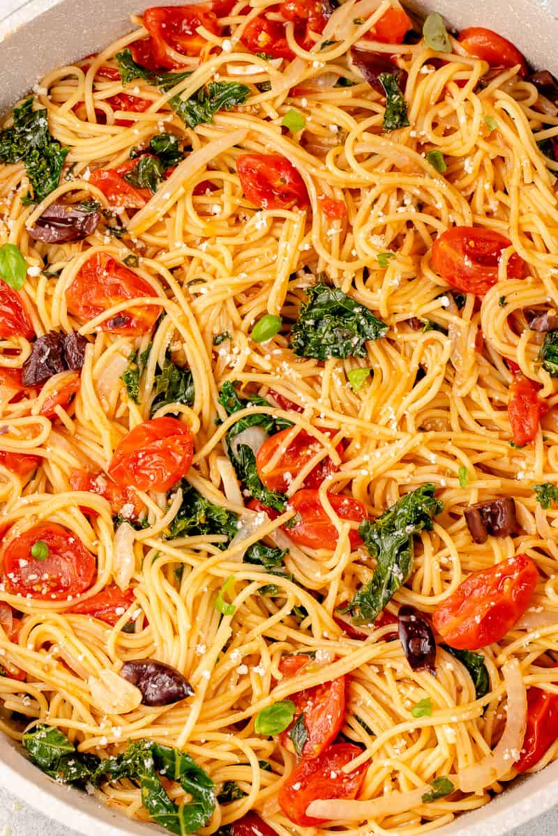 close up of vegan pasta in a pot with tomatoes, kale, olives, basil and parmesan