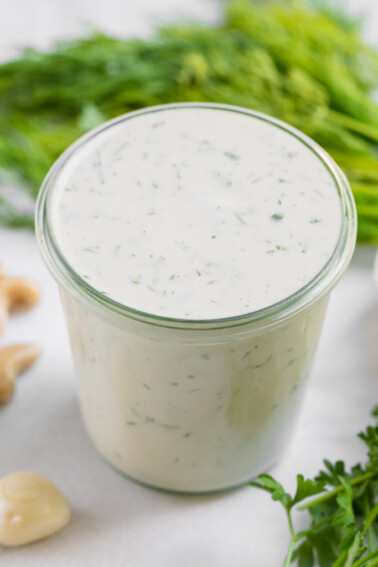 Cashew ranch dressing in a cup surrounded by ingredients by sweet simple vegan