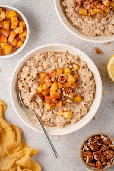 Overhead image of apple cinnamon oatmeal in bowl with a spoon styled on a grey background