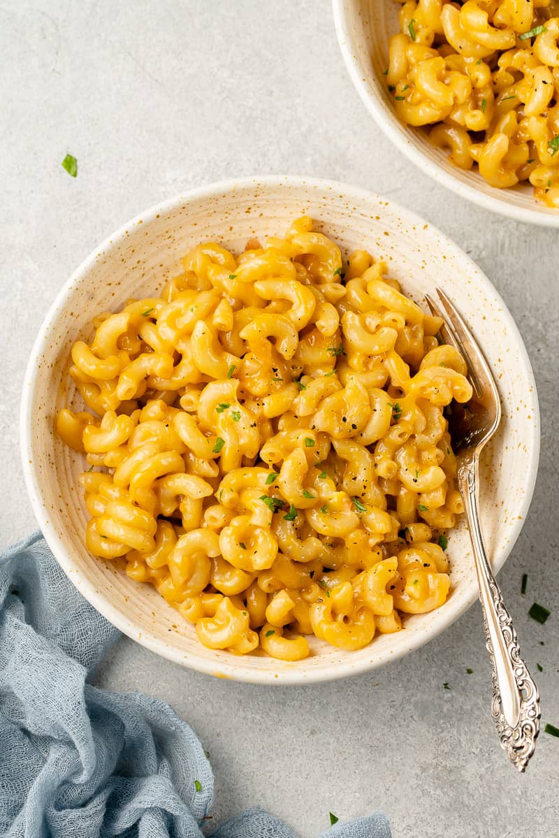 a close up of vegan mac and cheese in a white bowl with a fork
