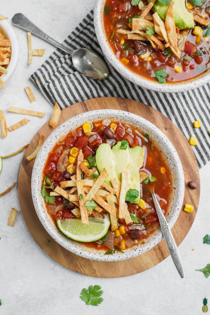 A bowl of vegan tortilla soup with garnishes and a spoon