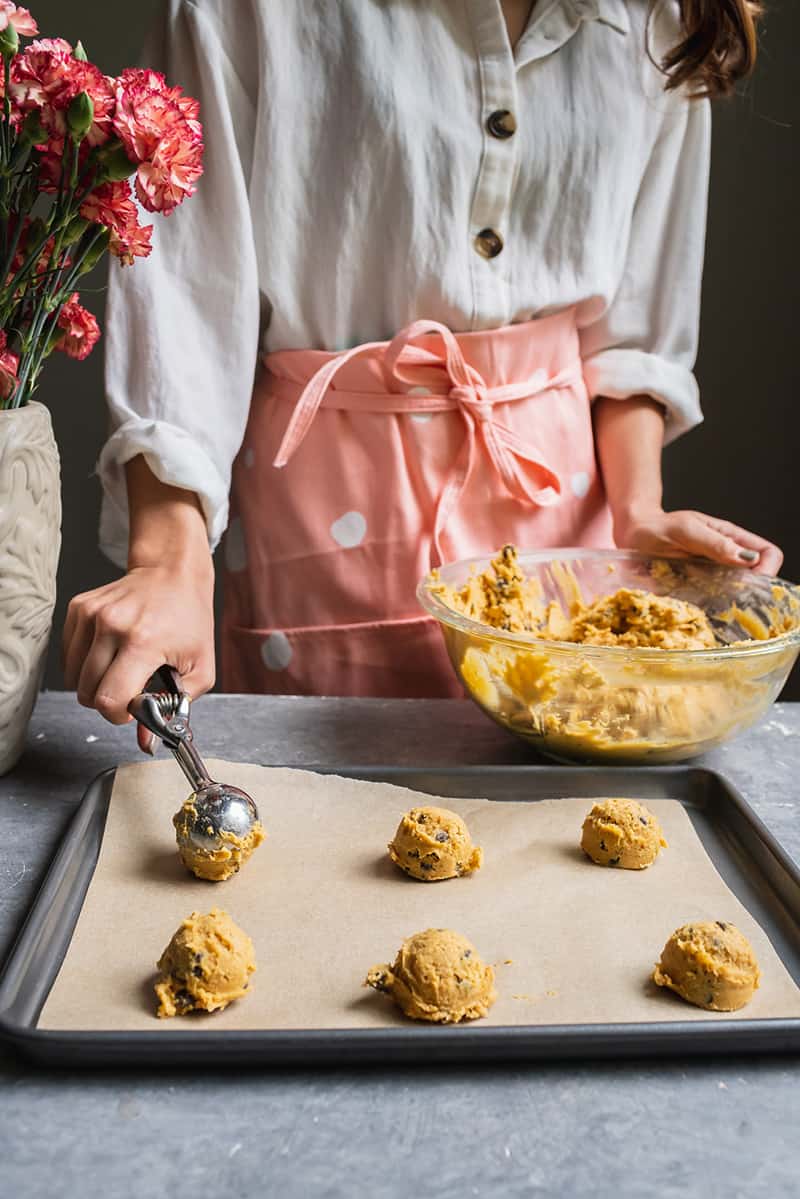 woman scooping mounds of pumpkin chocolate chip cookies onto lined baking sheet