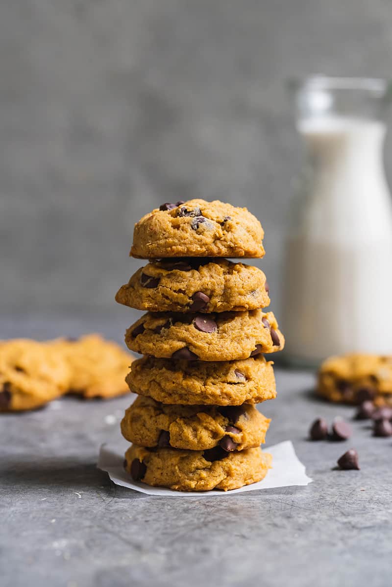 a stack of pumpkin chocolate chip cookies on gray board with cup of milk