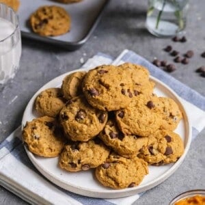 a white plate of pumpkin chocolate chip cookies on gray board with cup of milk