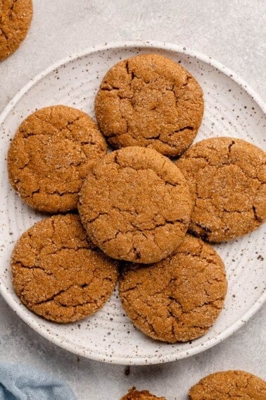 overhead shot of vegan ginger molasses cookies on a white speckled plate with a blue towel