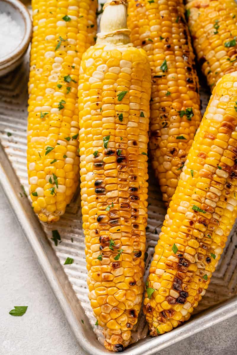 grilled corn on a baking sheet with butter and parsley