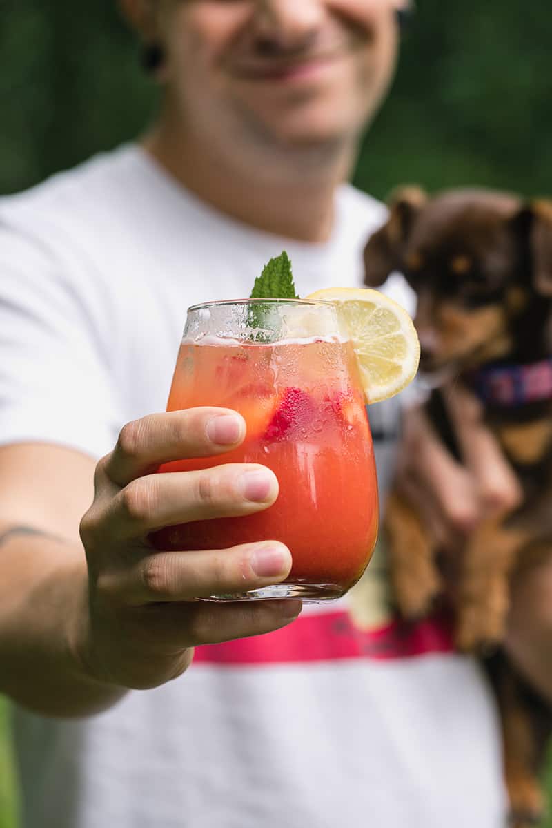 a man holding a cup of strawberry lemonade with his dog in his other arm