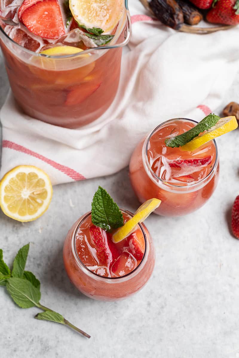 overhead photos of two glasses of strawberry lemonade on white table with full pitcher in the background