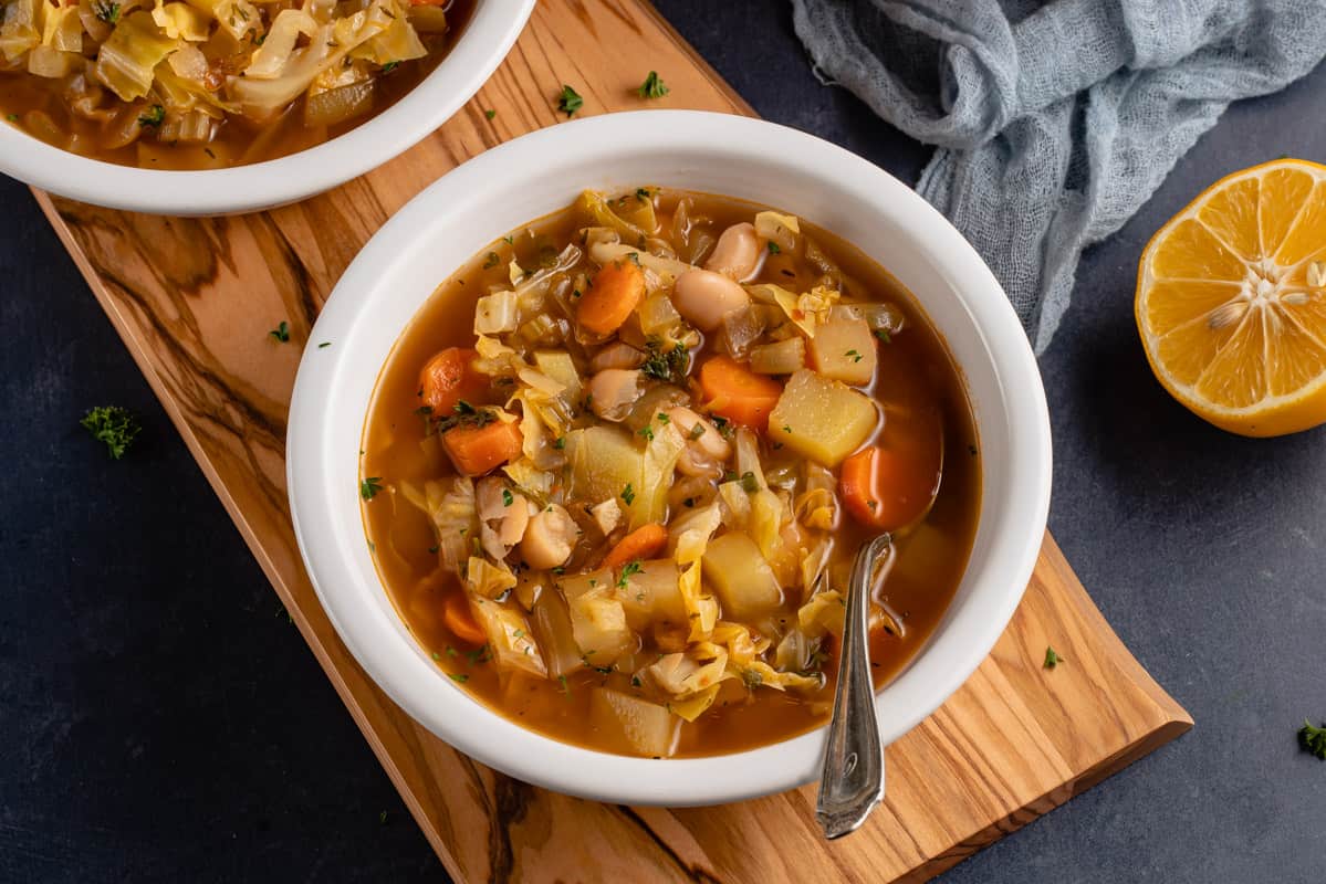 horizontal photo of white bowl with vegan cabbage soup and metal spoon
