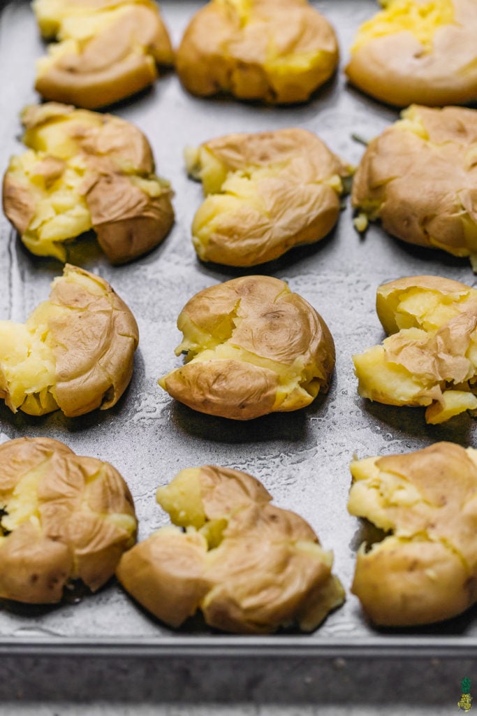 Smashed potatoes on a baking sheet before being seasoned and baked until crispy by sweet simple vegan