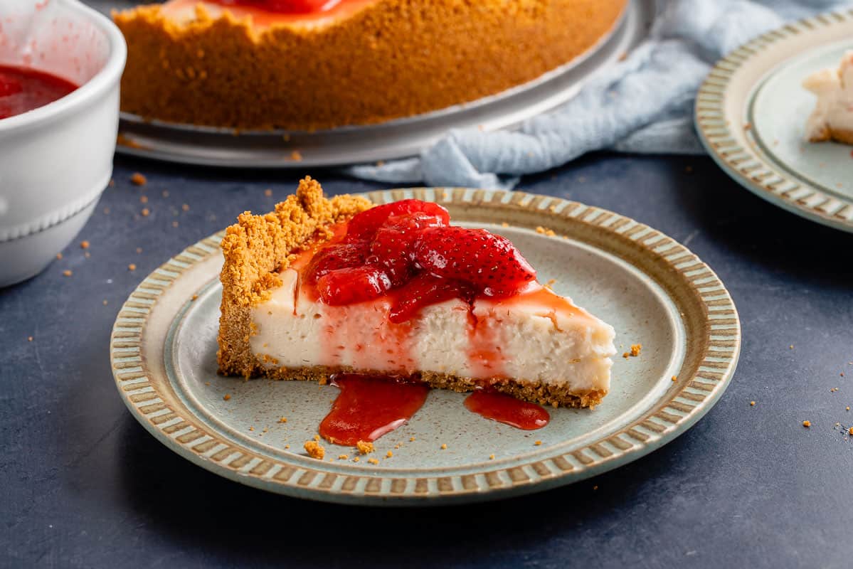 horizontal photo of vegan cheesecake with strawberry sauce on light blue plate