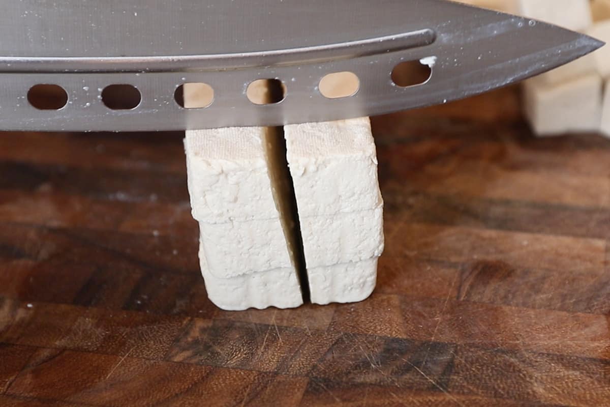dicing pressed tofu on wooden cutting board