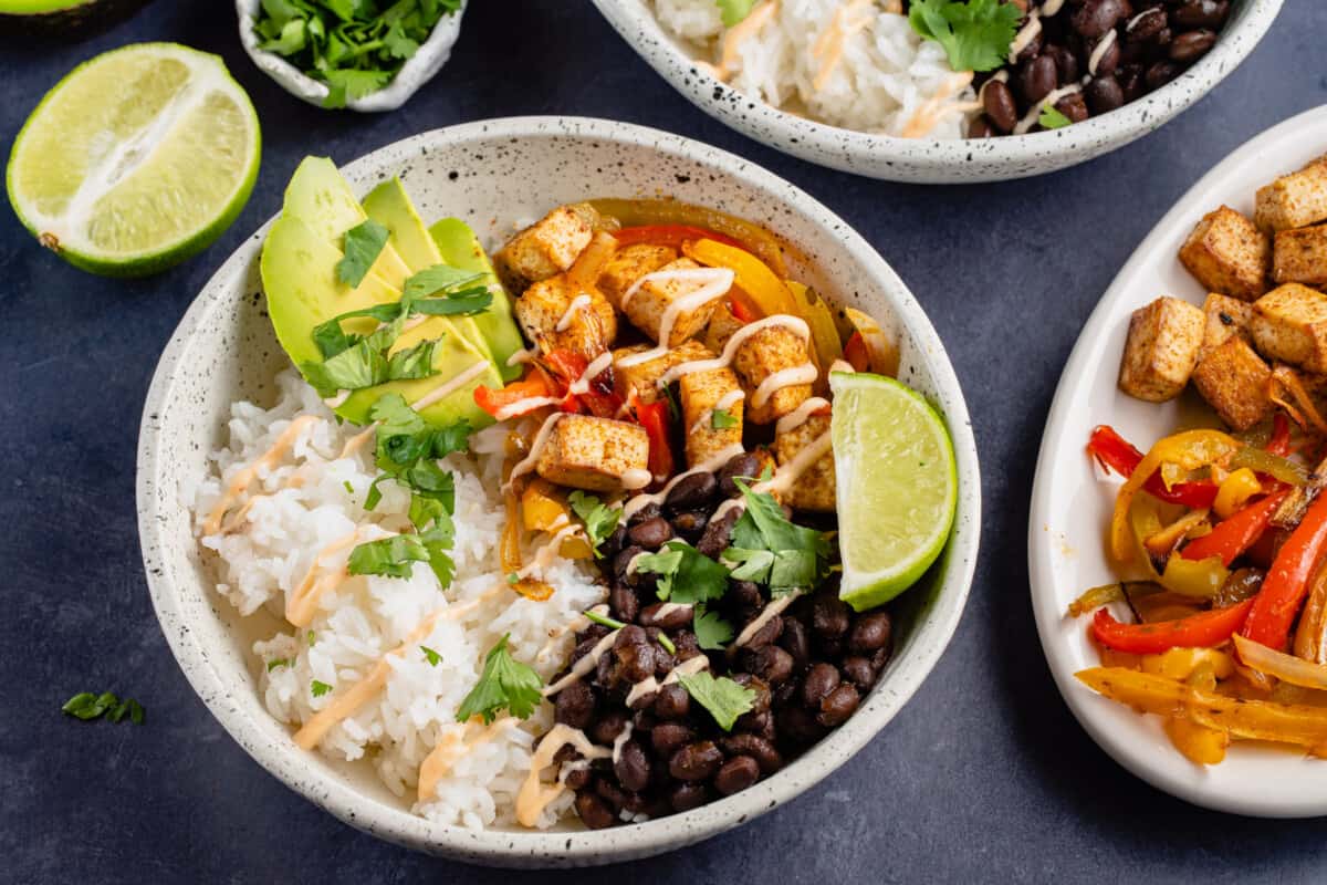 horizontal photo of white bowl of tofu fajitas with black beans, lime and chipotle cream