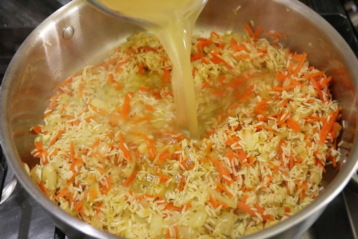 broth being poured over rice and carrots