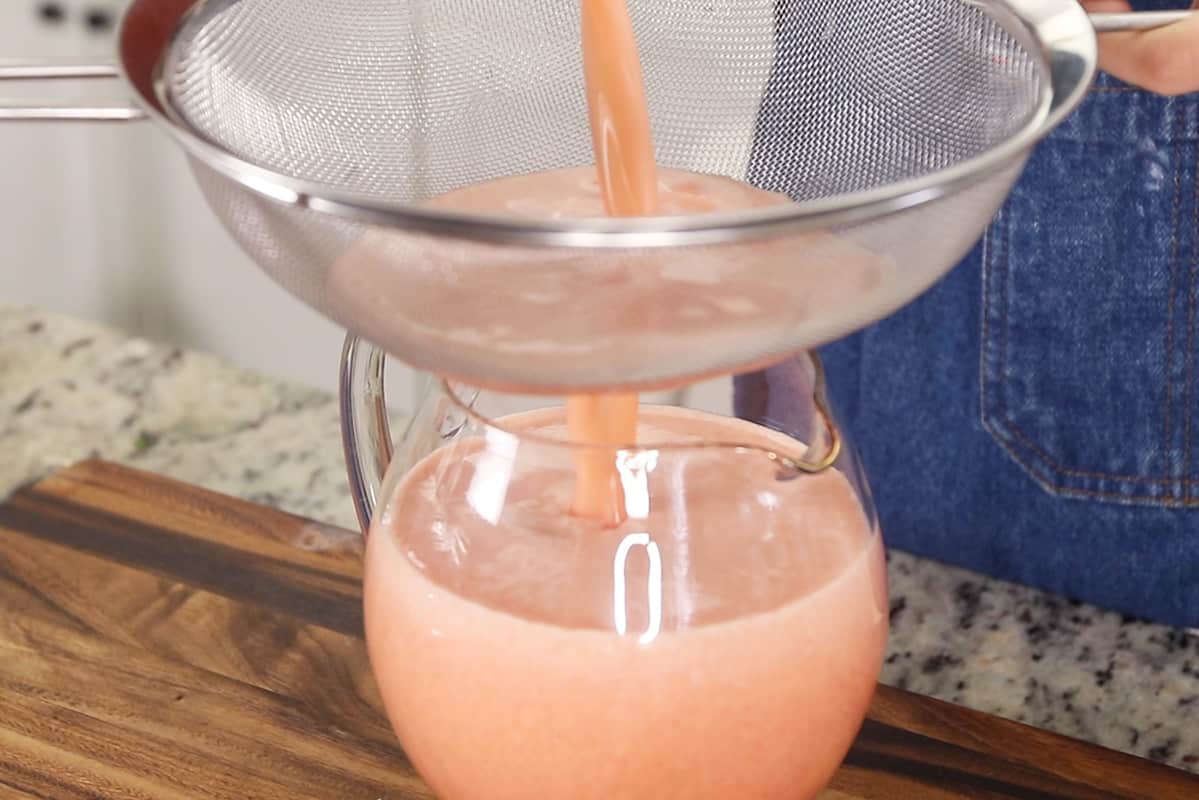 straining homemade strawberry lemonade into pitcher