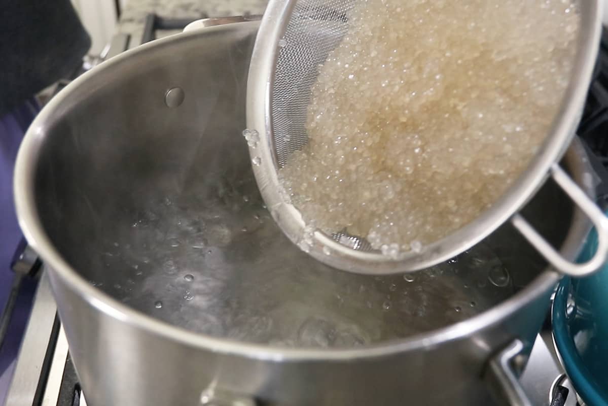 pouring parboiled tapioca pearls into boiling water in stainless steel pot