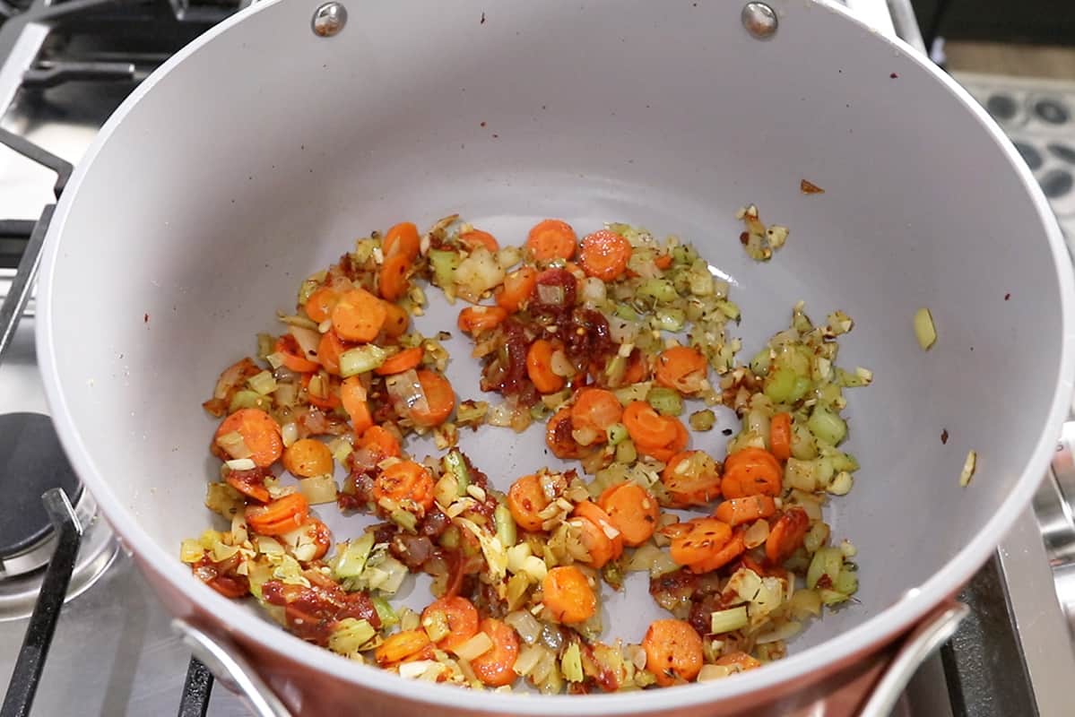 sautéing mirepoix and tomato paste in large gray caraway pot