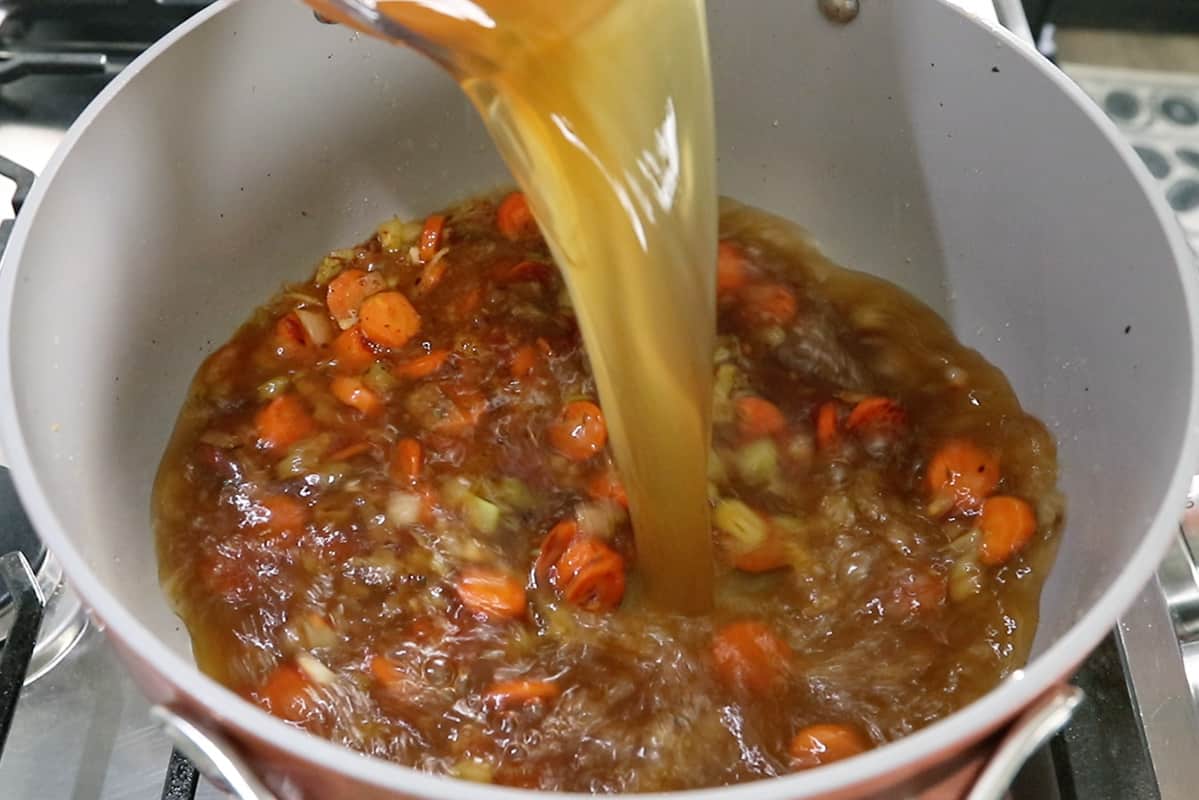 pouring vegetable broth into cabbage soup in gray pot