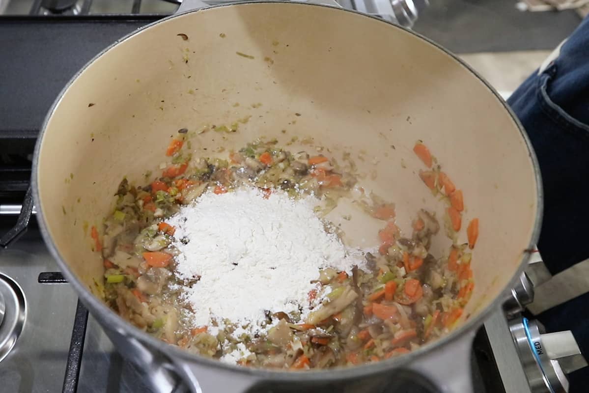 adding flour to large pot of sautéed vegetables for chowder