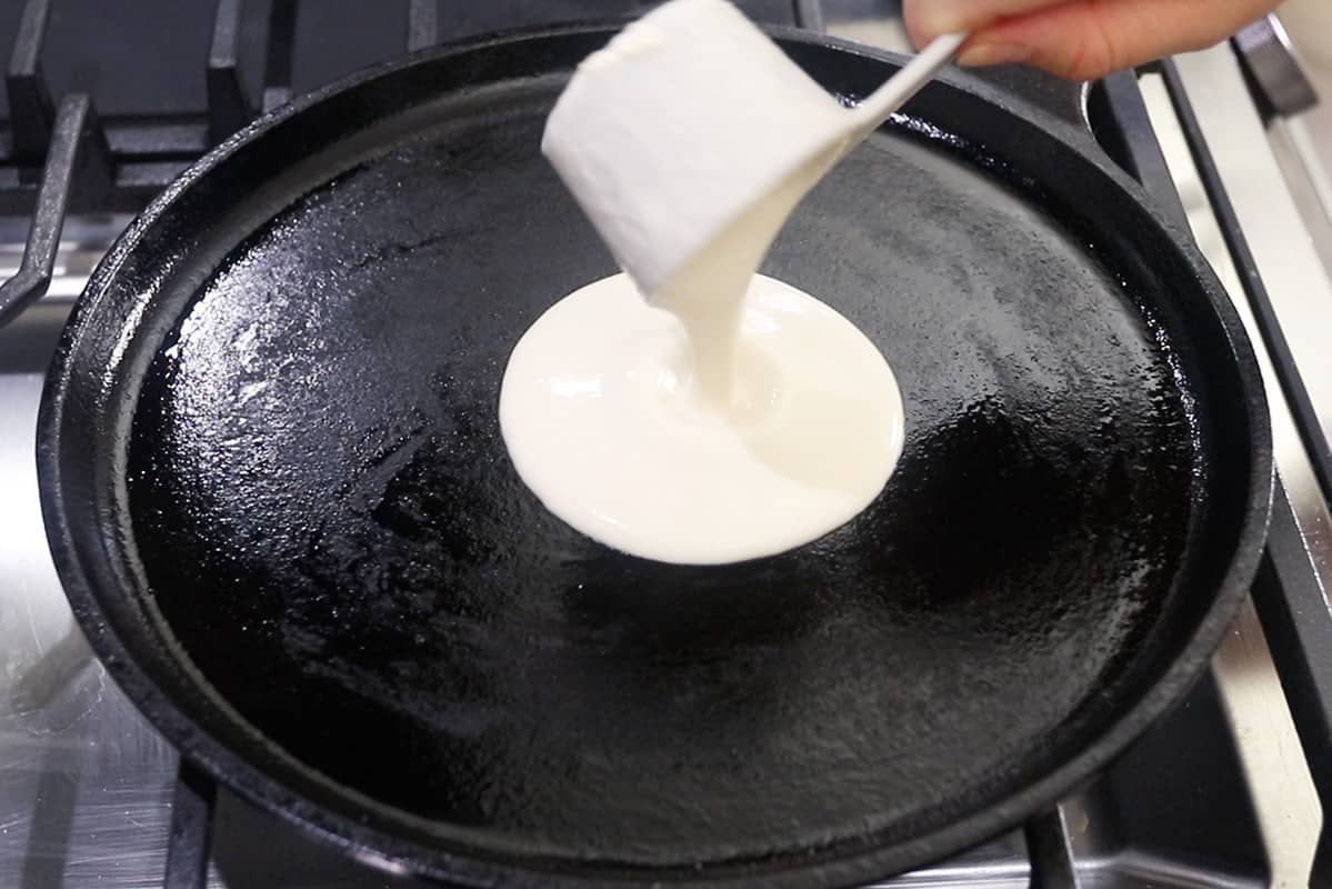 pouring crepe batter onto cast iron griddle pan