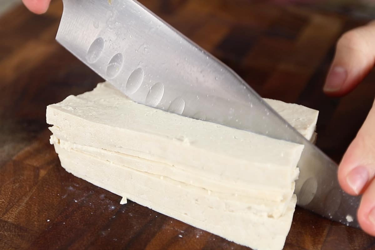 slicing super firm tofu on wooden cutting board