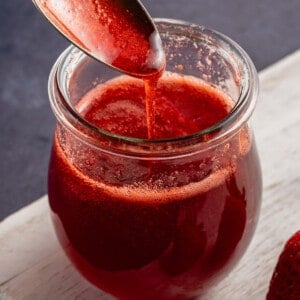 scooping strawberry syrup with metal spoon in glass jar