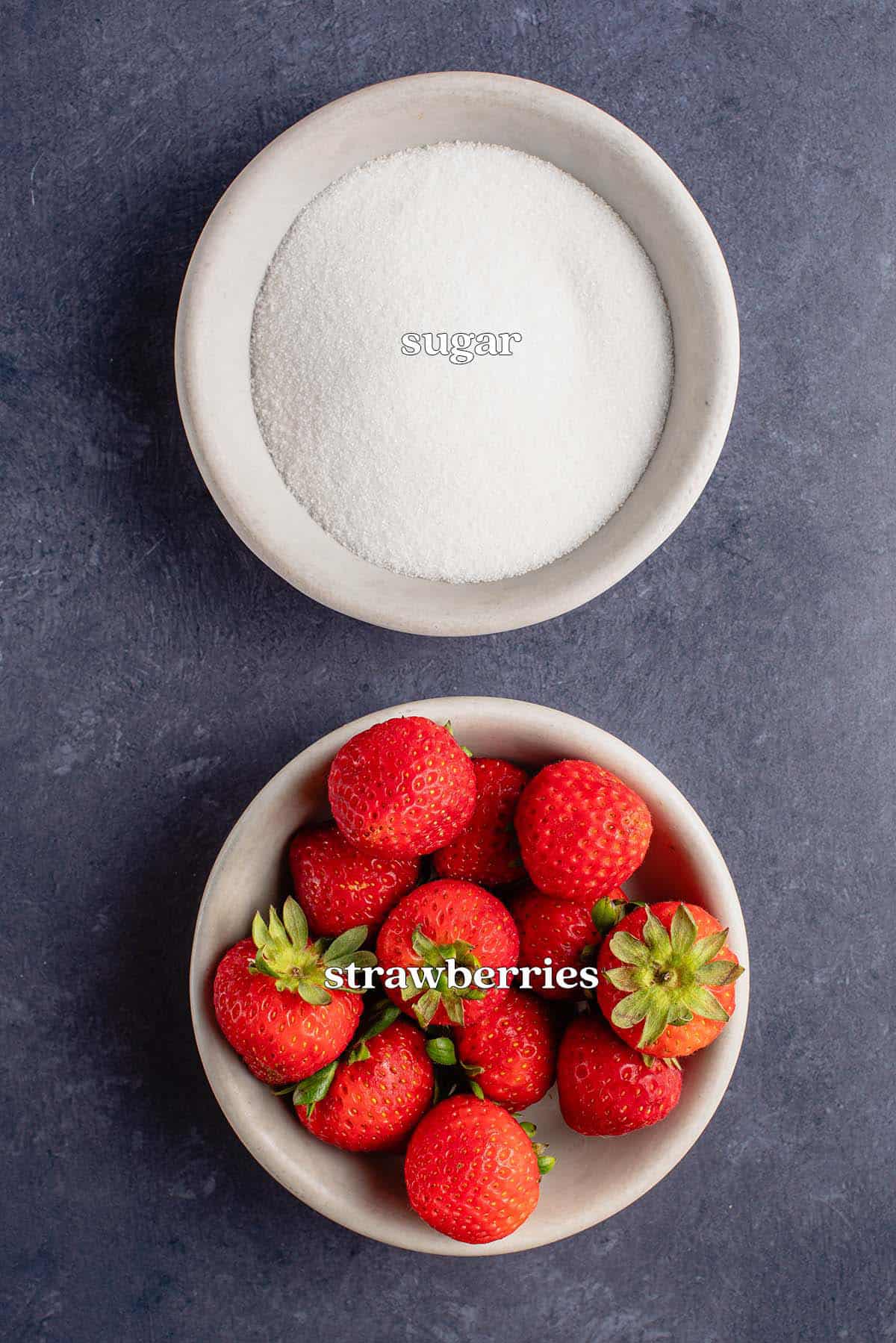 strawberries and sugar in bowls on blue board