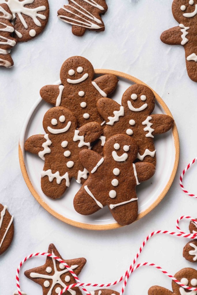 an overhead shot of gingerbread cookies with white icing on a plate on a marble background with red string