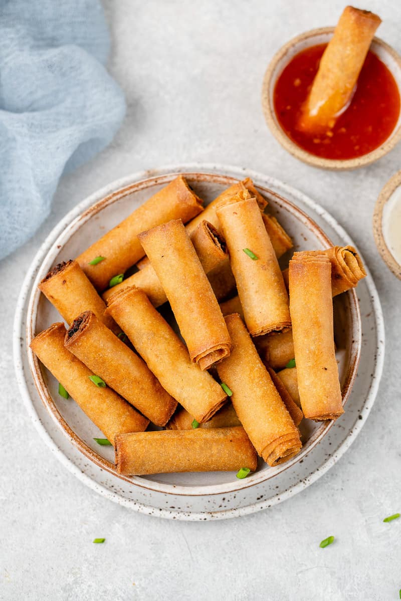 shot of Filipino Lumiang Shanghai (vegan spring rolls) in a white bowl with dipping sauces by sweet simple vegan