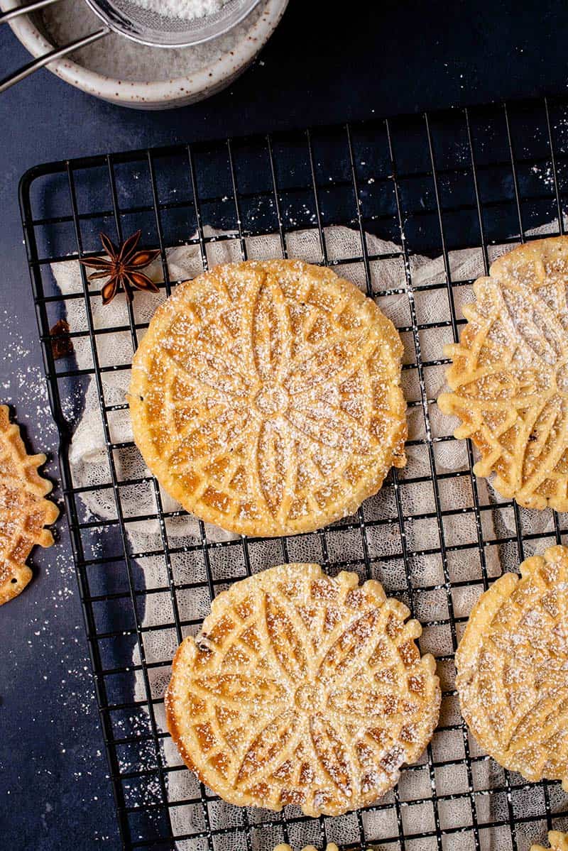 overhead image of pizzelles on a cooling rack dusted with powdered sugar