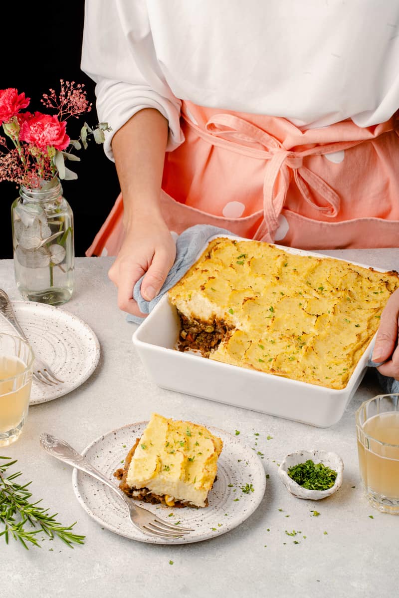 lifestyle image holding shepherds pie baking dish with piece taken out of it