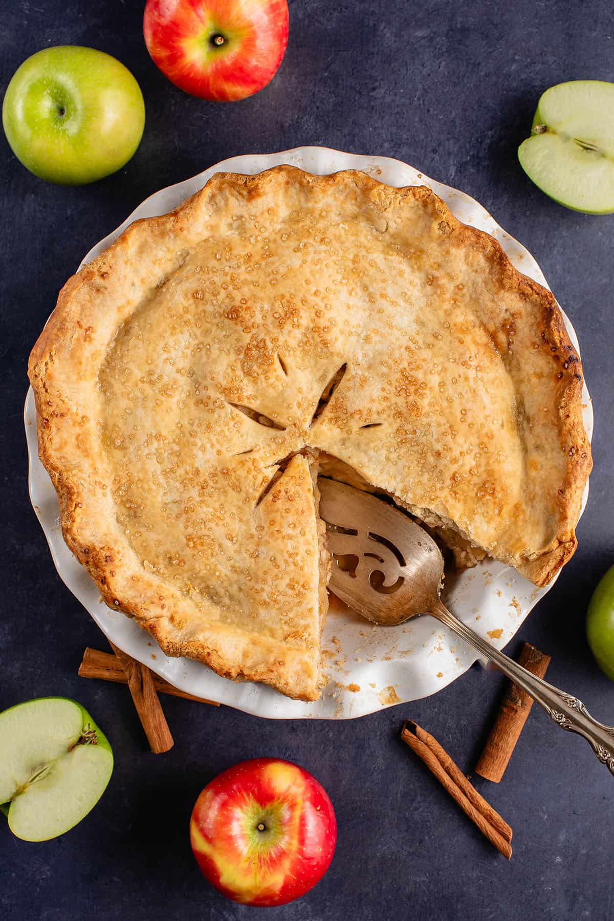 Overhead shot of slices apple pie with serving utensil on blue background