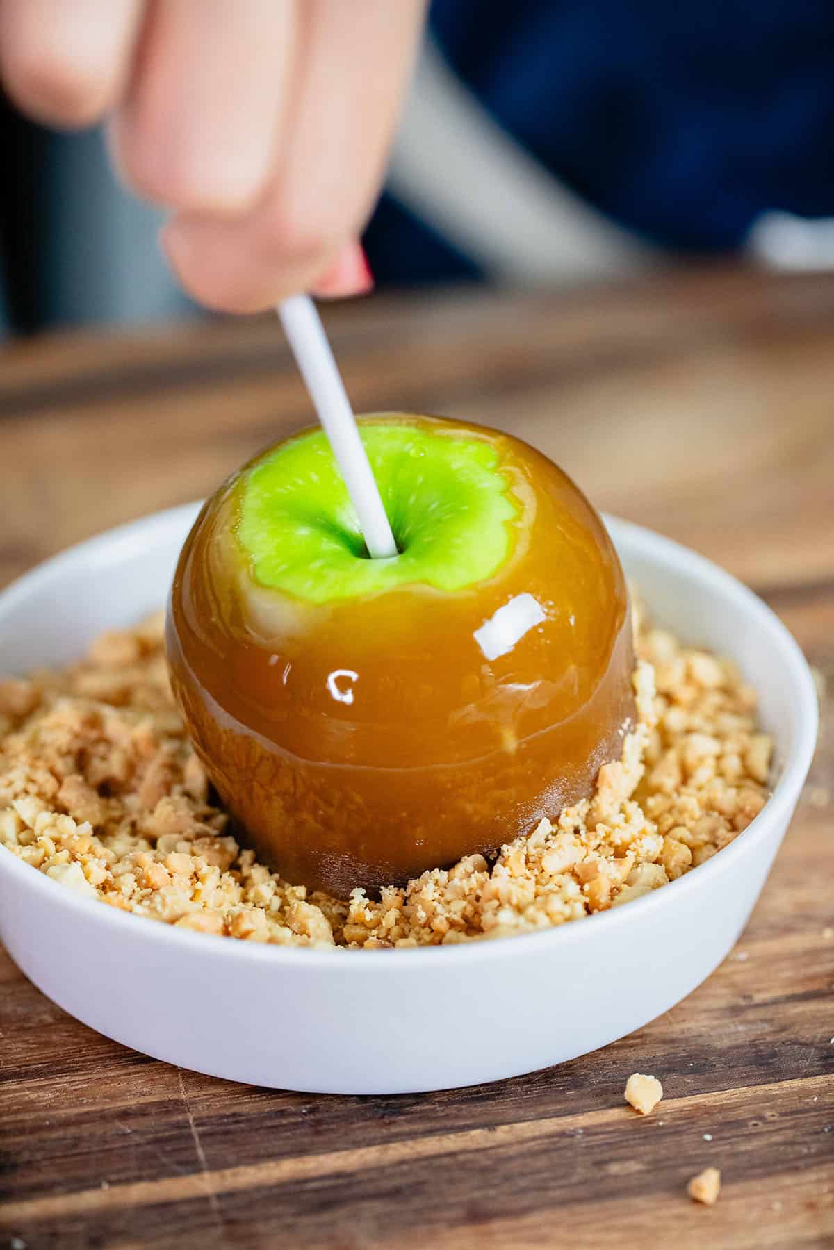 caramel apple being dipped into crushed peanuts