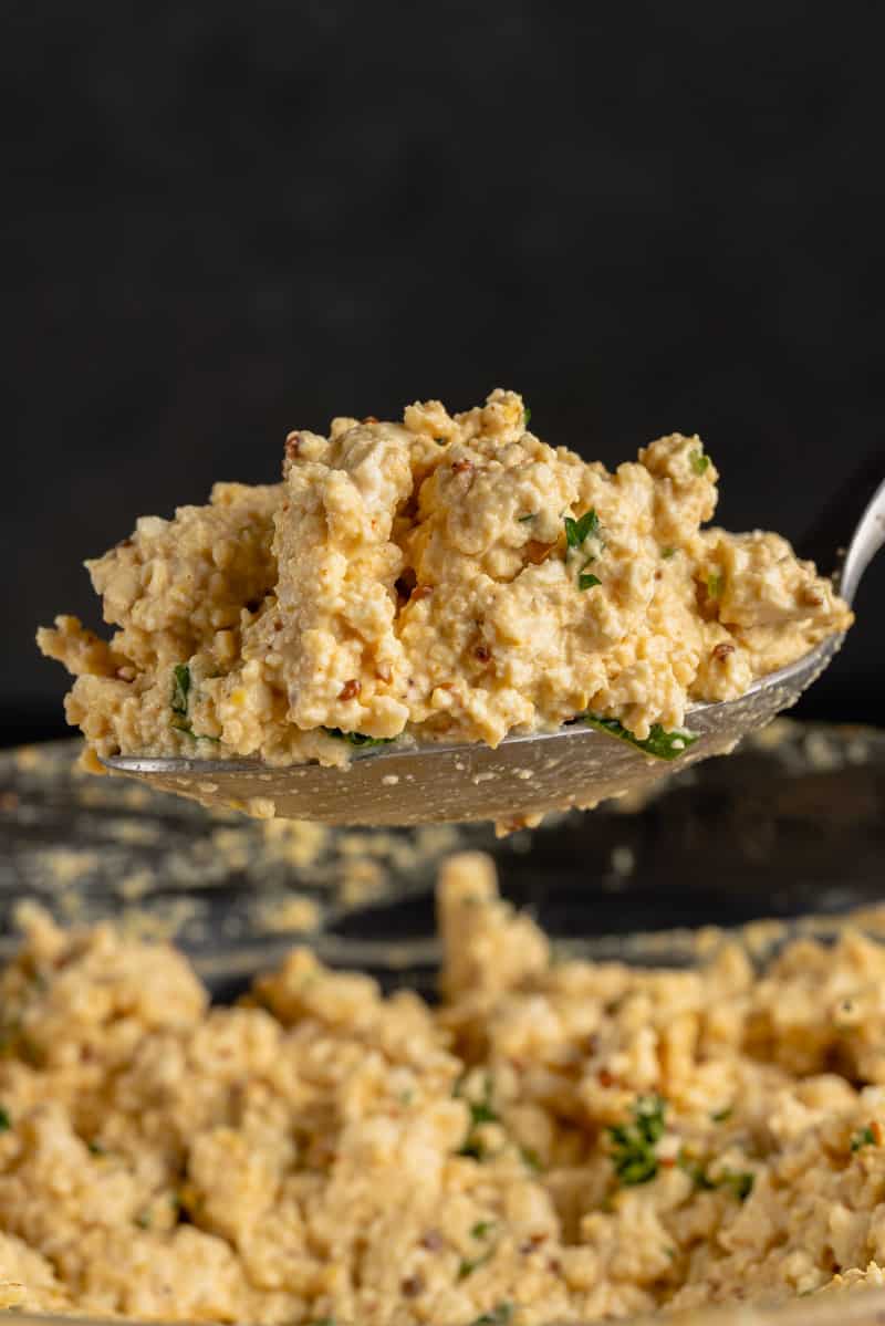 close up of spoon full of vegan tofu egg salad on blue table