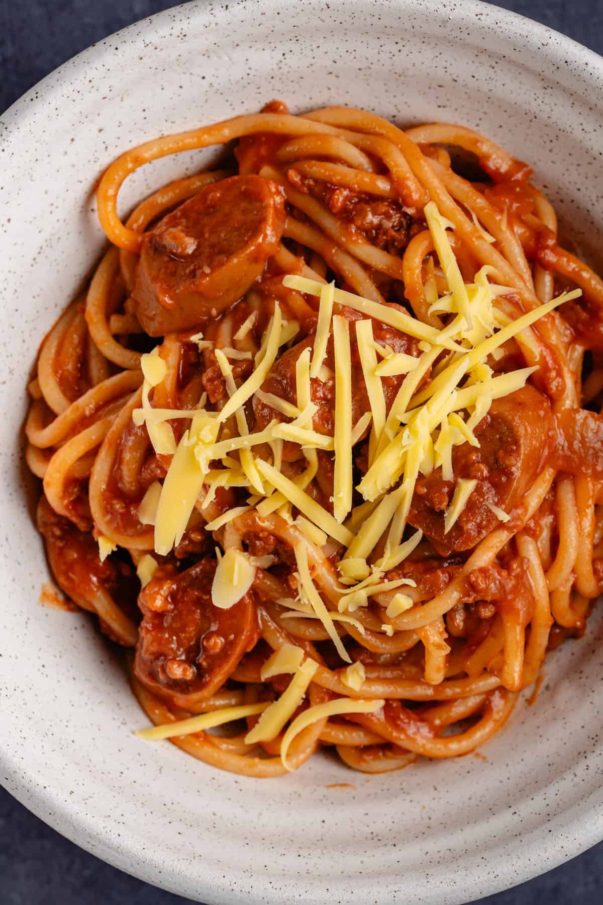 vegan filipino spaghetti with cheddar cheese in white bowl