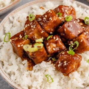 close up of saucy vegan generalo tso's tofu in a bowl with rice