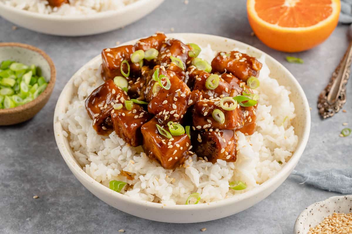 close up of saucy vegan orange tofu in a bowl with rice