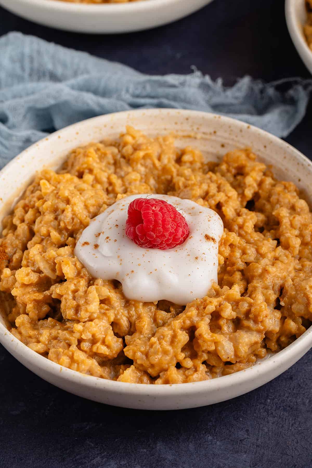 bowl of pumpkin rice pudding with a dollop of cream and a raspberry